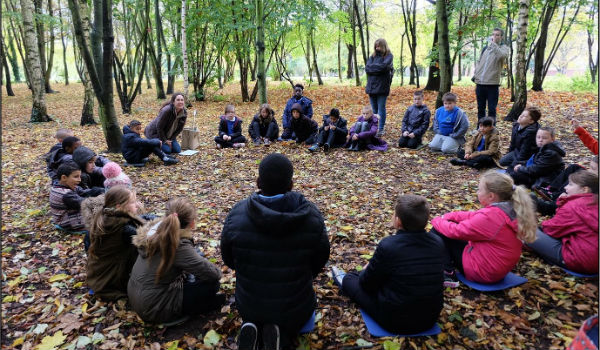 Group of people sat in a circle in the woodland in autumn.
