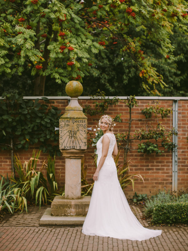 Bride in wedding dress stood in garden next to sundial.