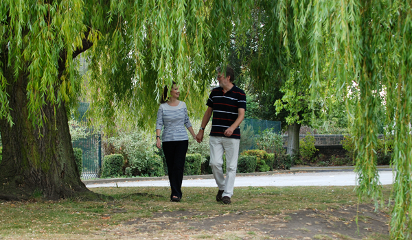 Man and woman walking on path underneath large tree