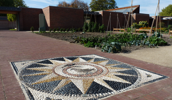 Pebbled mosaic in a walled garden with vegetable patch in the background 